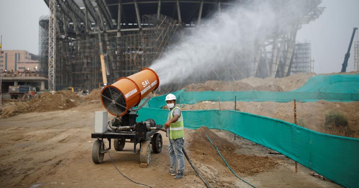 Anti-smog gun spraying water mist at a barricaded construction site in Delhi with green dust-control netting — mandatory compliance under CPCB norms