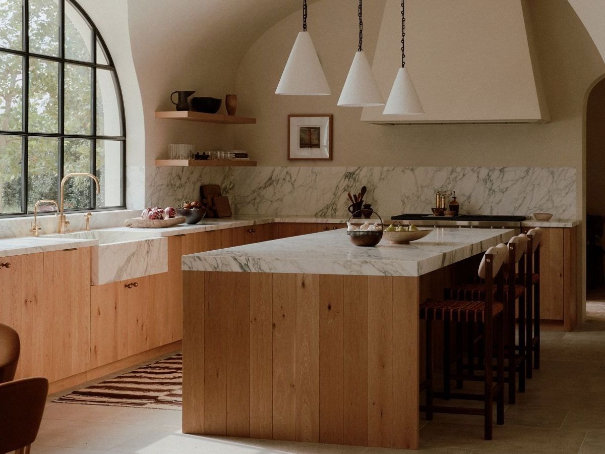Designer marble island kitchen interior by Evas Designs in Gurgaon — warm oak cabinetry, stone counters and an arched steel-framed window